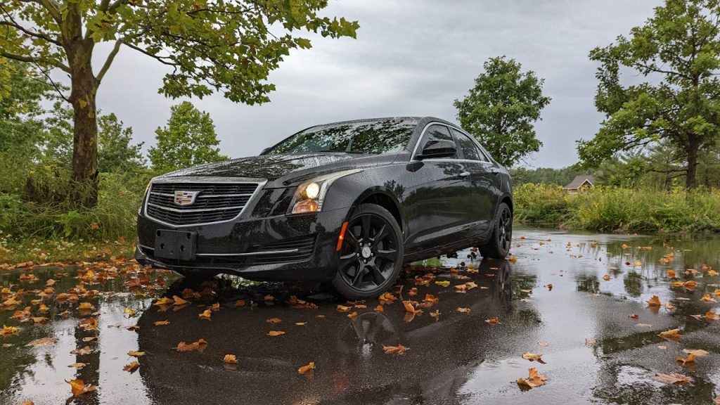 Corporate Car Service in Minnepolis. Elegant black Cadillac parked on a wet road with autumn leaves, showcasing luxury automotive design.