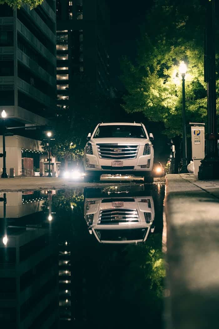 Reflection of a Cadillac Escalade in a rain puddle, symbolizing the polished, high class nighttime chauffeur experience offered by Chris and CMB Transport in the Twin Cities