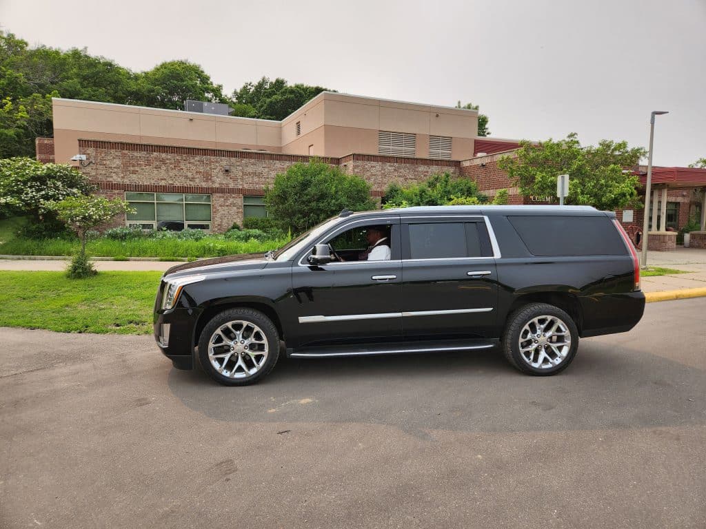 Minneapolis black car service
. CMB Transport chauffeur in black Cadillac Escalade SUV parked at commercial building, providing luxury executive transportation across Minnesota.