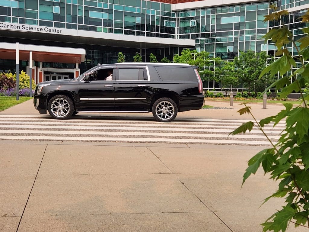 CMB Transport’s luxury Cadillac Escalade positioned in front of a modern business complex, perfect for corporate chauffeur services in Minneapolis and Twin Cities.